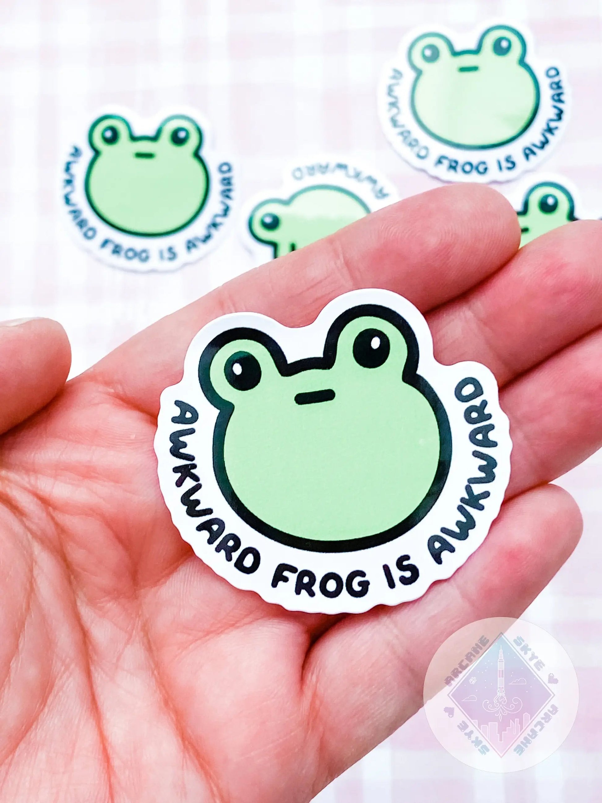 a hand holding a sticker with a frog on it