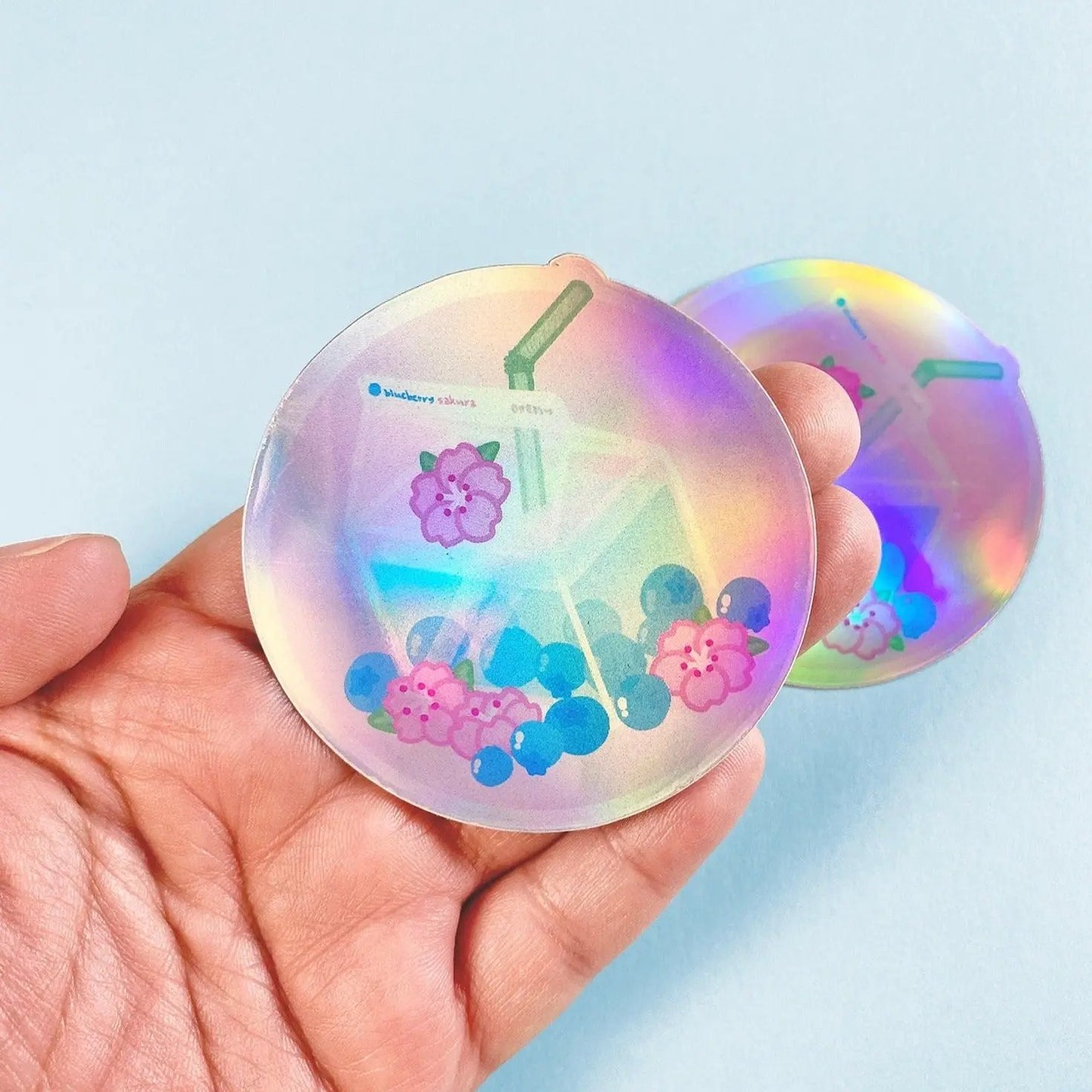 a hand holding two holographic discs with flowers on them