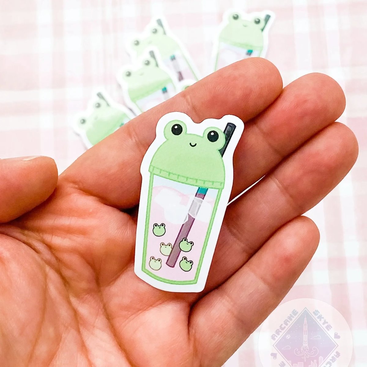a hand holding a sticker with a frog on it